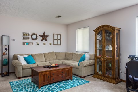 A living room with a beige couch, a wooden coffee table, and a glass cabinet.