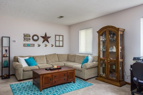 A living room with a beige couch, a wooden coffee table, and a glass cabinet.