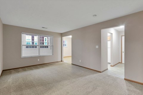 A spacious room with a carpeted floor and a window with blinds.