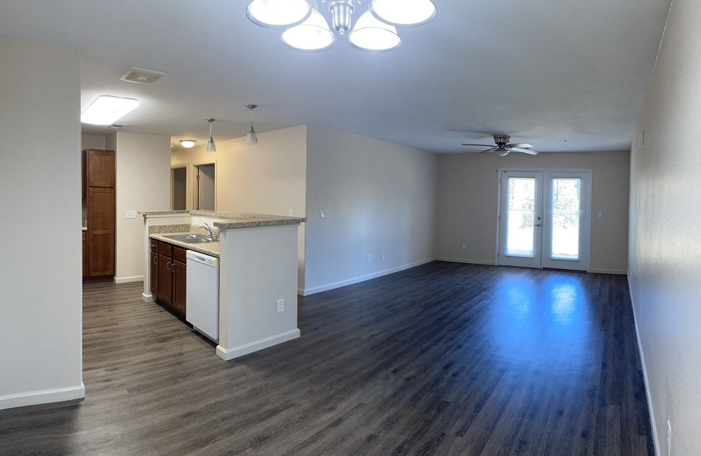 an empty living room with a kitchen and a ceiling fan