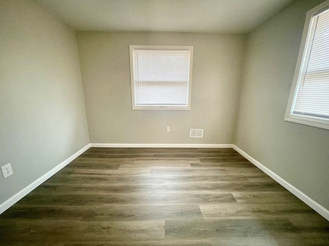 a empty room with wooden floors and two windows