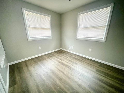 an empty room with wood floors and two windows