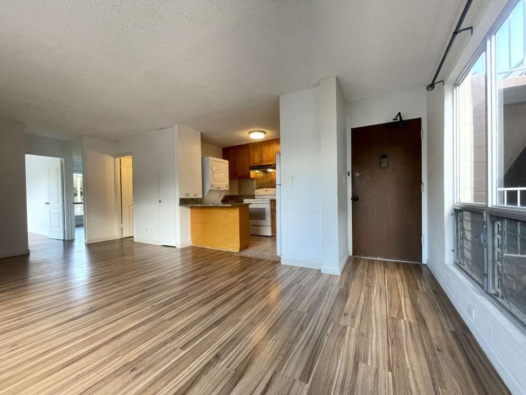 A room with wooden flooring and a kitchen area in the background.