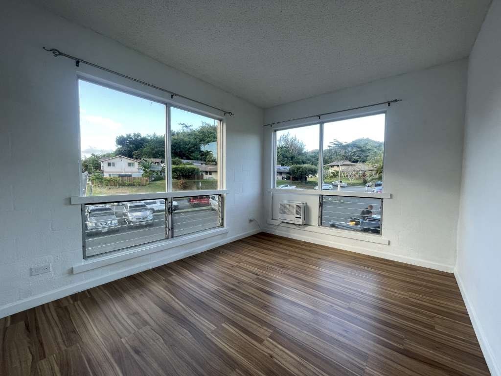 A room with wooden floors and a view of a parking lot through the windows.