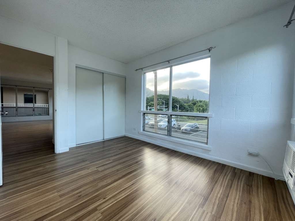 A room with wooden flooring and a window overlooking a parking lot.