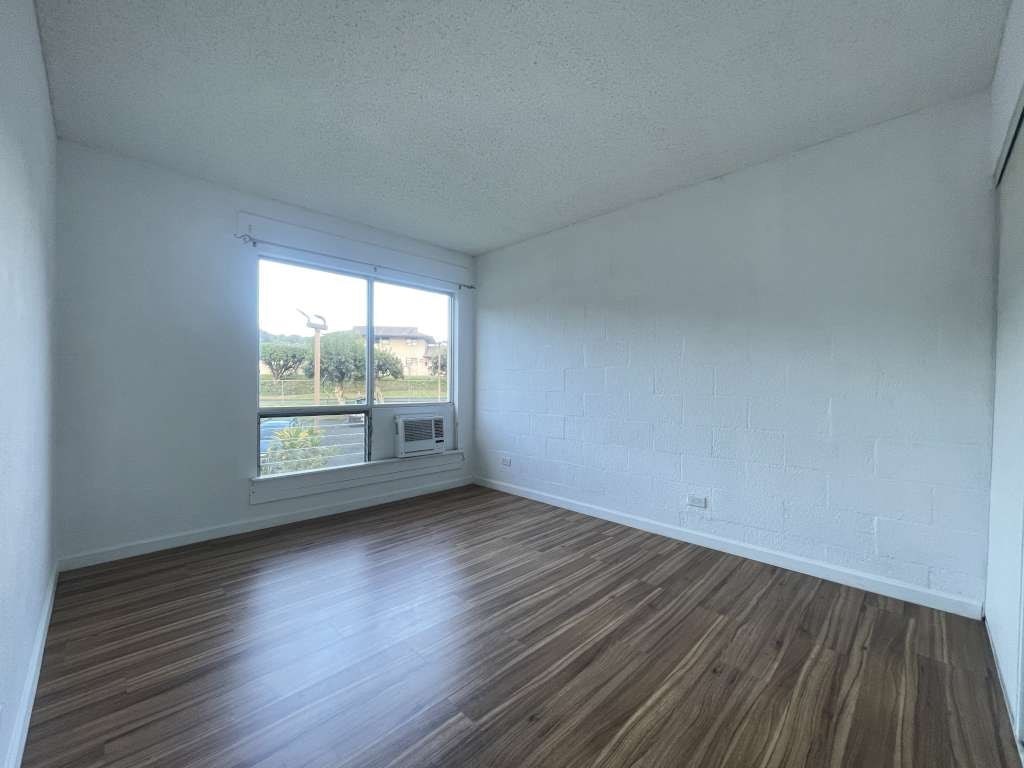 A room with wooden flooring and a window overlooking a green area.