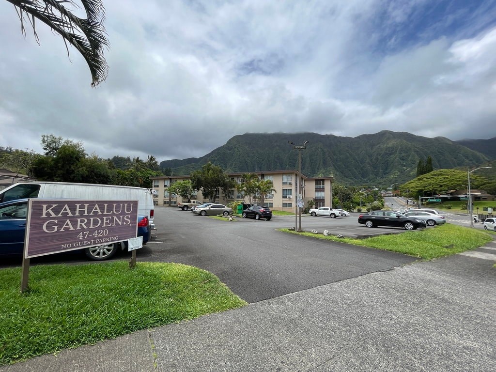 A sign for Kahalu'u Gardens is in the foreground of a cloudy day.