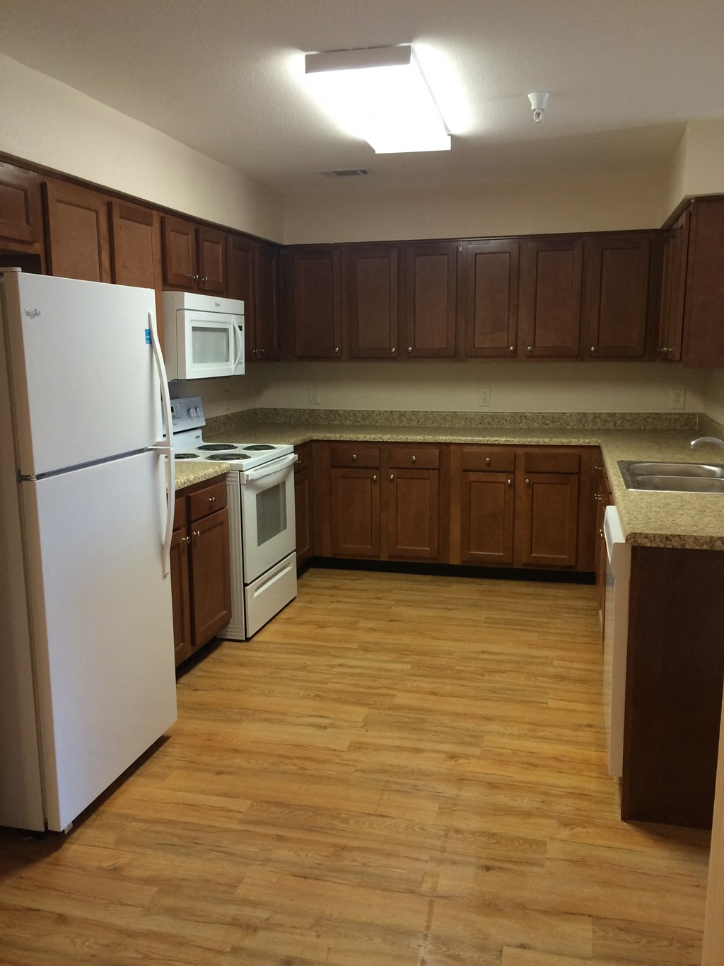 an empty kitchen with wooden floors and white appliances