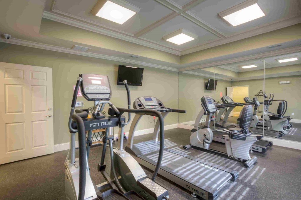 a gym with cardio machines and a tv