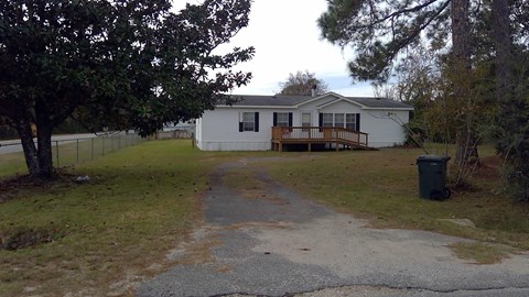 a small white house with a driveway and a deck