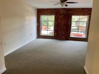 an empty living room with a ceiling fan and a brick wall