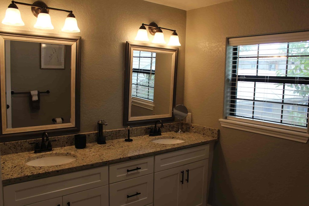 a bathroom with two sinks and two mirrors and a window