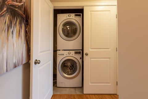 A white door is open to reveal a white washing machine in a laundry room.
