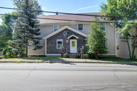 A house with a grey facade and a green door is surrounded by trees.