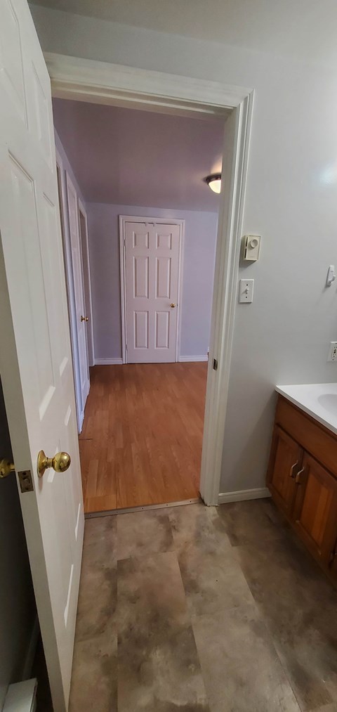 A white door with a gold handle is open to a room with a white wall and a white door with a white frame.