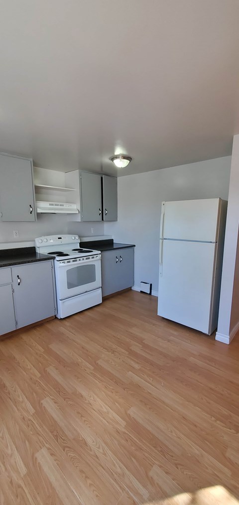 A kitchen with a white fridge and wooden floors.