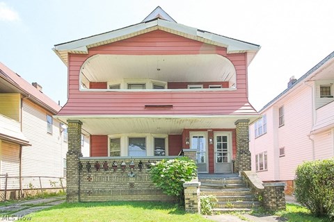 A pink house with a white porch and a red door.