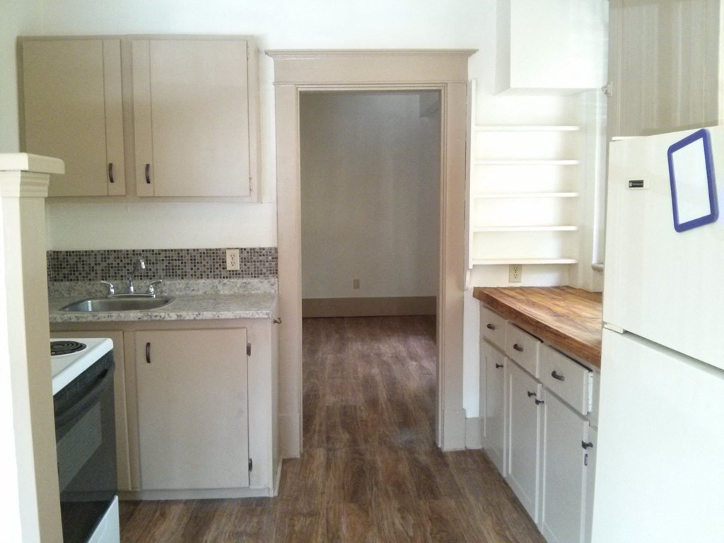 an empty kitchen with white cabinets and a door to the living room
