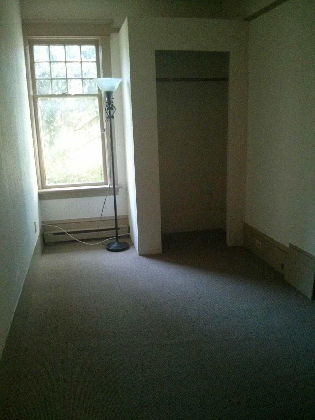 an empty room with a window and a floor lamp