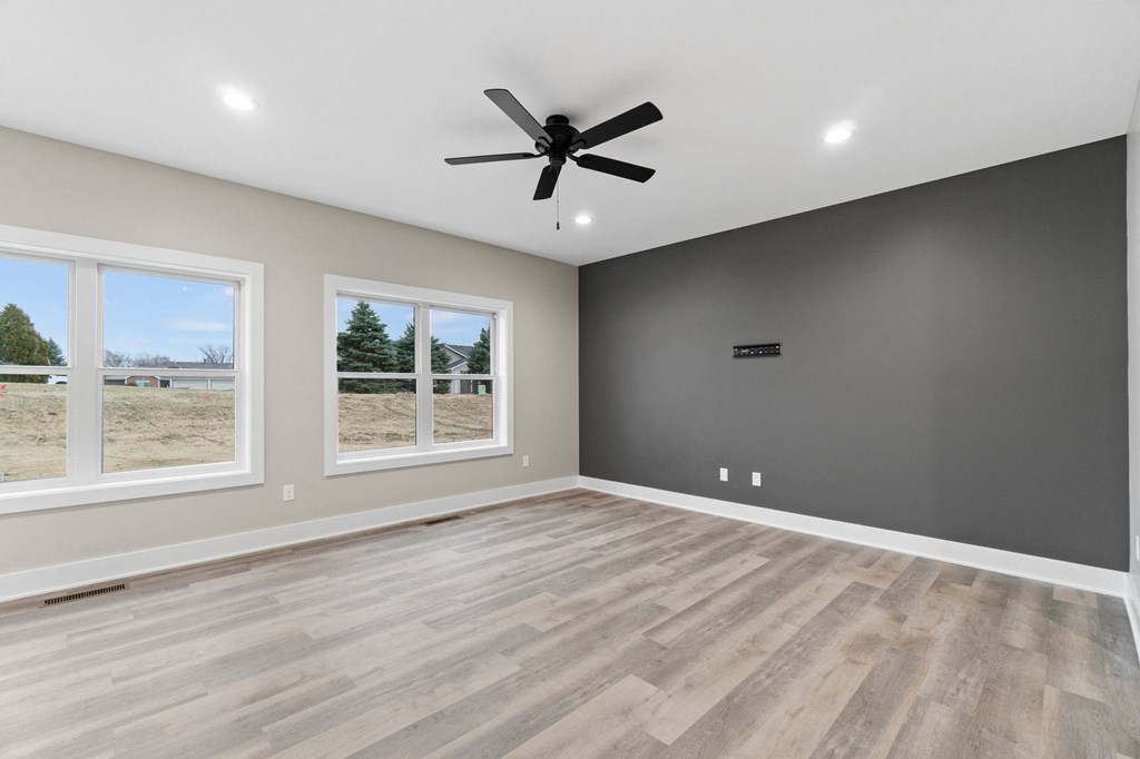 an empty living room with a ceiling fan and three windows