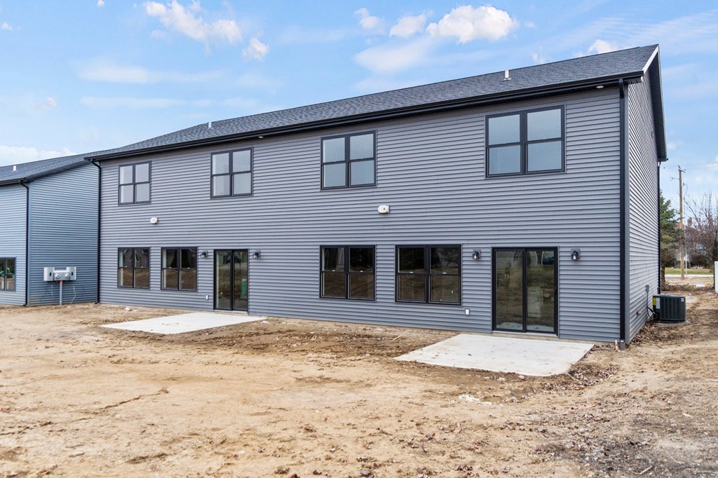 the back of a blue house with windows and a dirt field