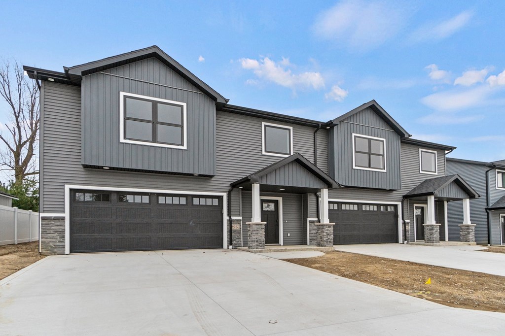 the front of a grey house with a driveway and garage doors