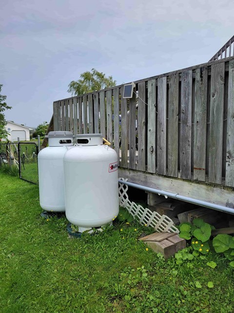 Two white containers are placed on the grass next to a wooden fence.