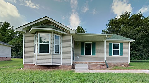 a small gray house with green shutters and grass and trees