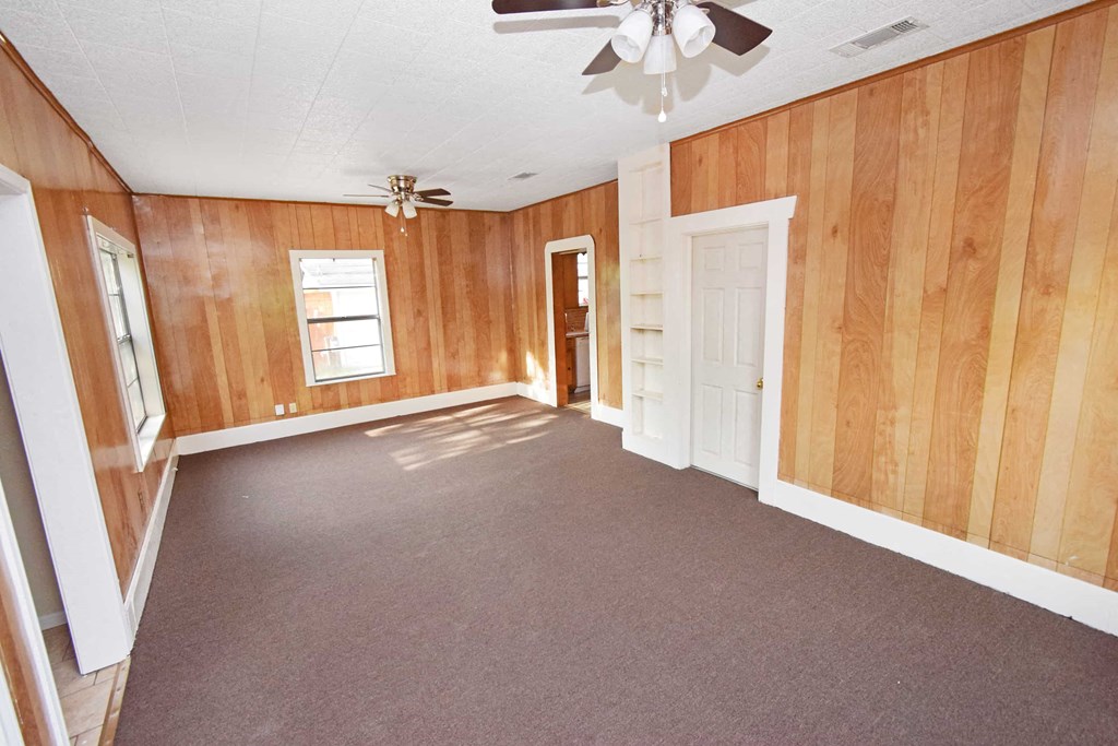 an empty living room with wood paneling and a ceiling fan