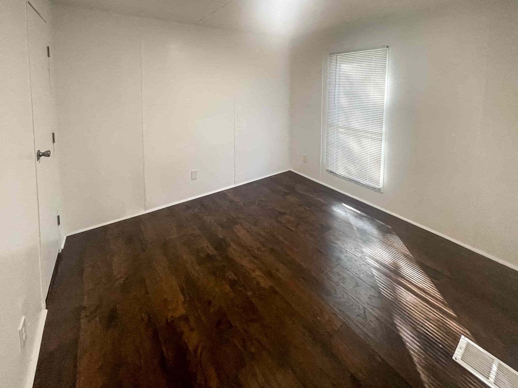 a room with a hard wood floor and white walls and a window