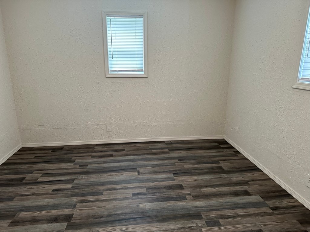 an empty room with wooden floors and two windows