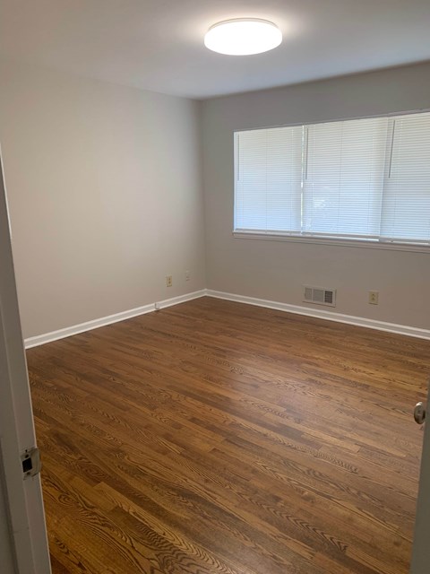 A room with wooden flooring and a window with blinds.