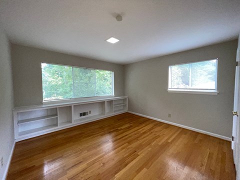 an empty room with a wood floor and two windows