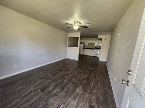 an empty living room with a ceiling fan and a kitchen