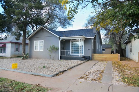 A grey house with a small front yard and a yellow sign.