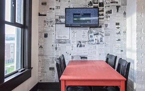 a dining room with a red table and black chairs and a wall covered in newspaper