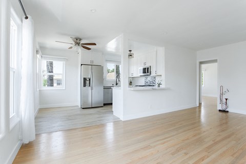 an empty living room with a kitchen and a ceiling fan