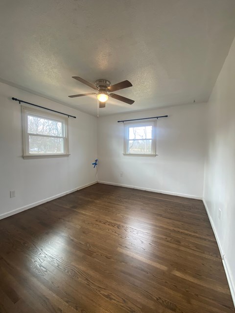 A room with a ceiling fan and two windows.