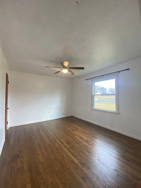 A room with a ceiling fan and a window showing a view of a grassy area outside.