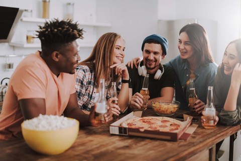 A group of people are gathered around a table with a bowl of popcorn and a pizza.
