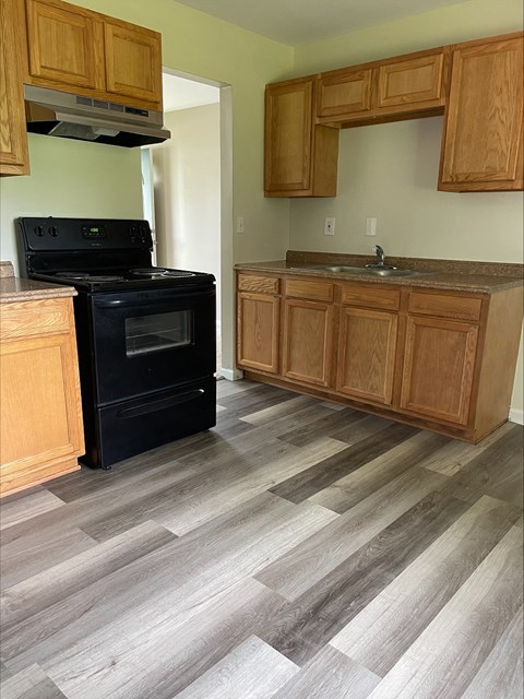 A black stove in a kitchen with wooden cabinets and a wooden floor.