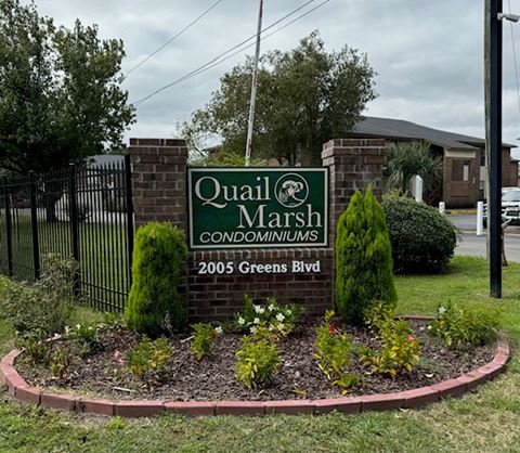 a sign for quail marsh condominiums in front of a garden