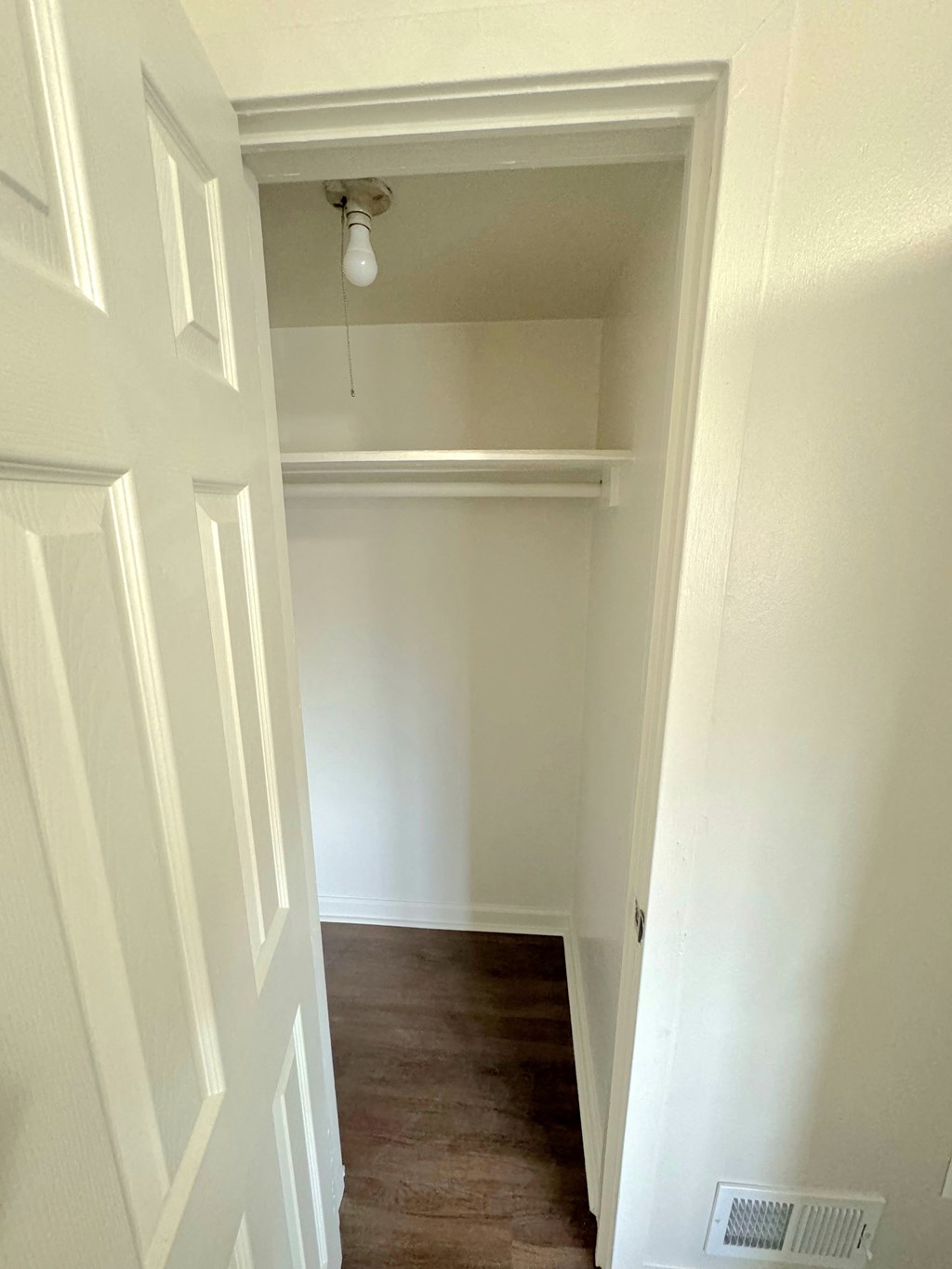 a walk in closet in a home with white walls and a wood floor