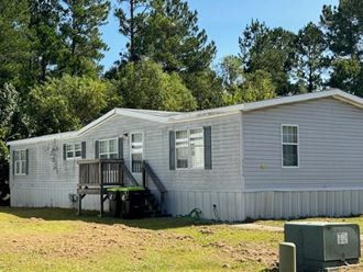 a white mobile home with a deck and trees