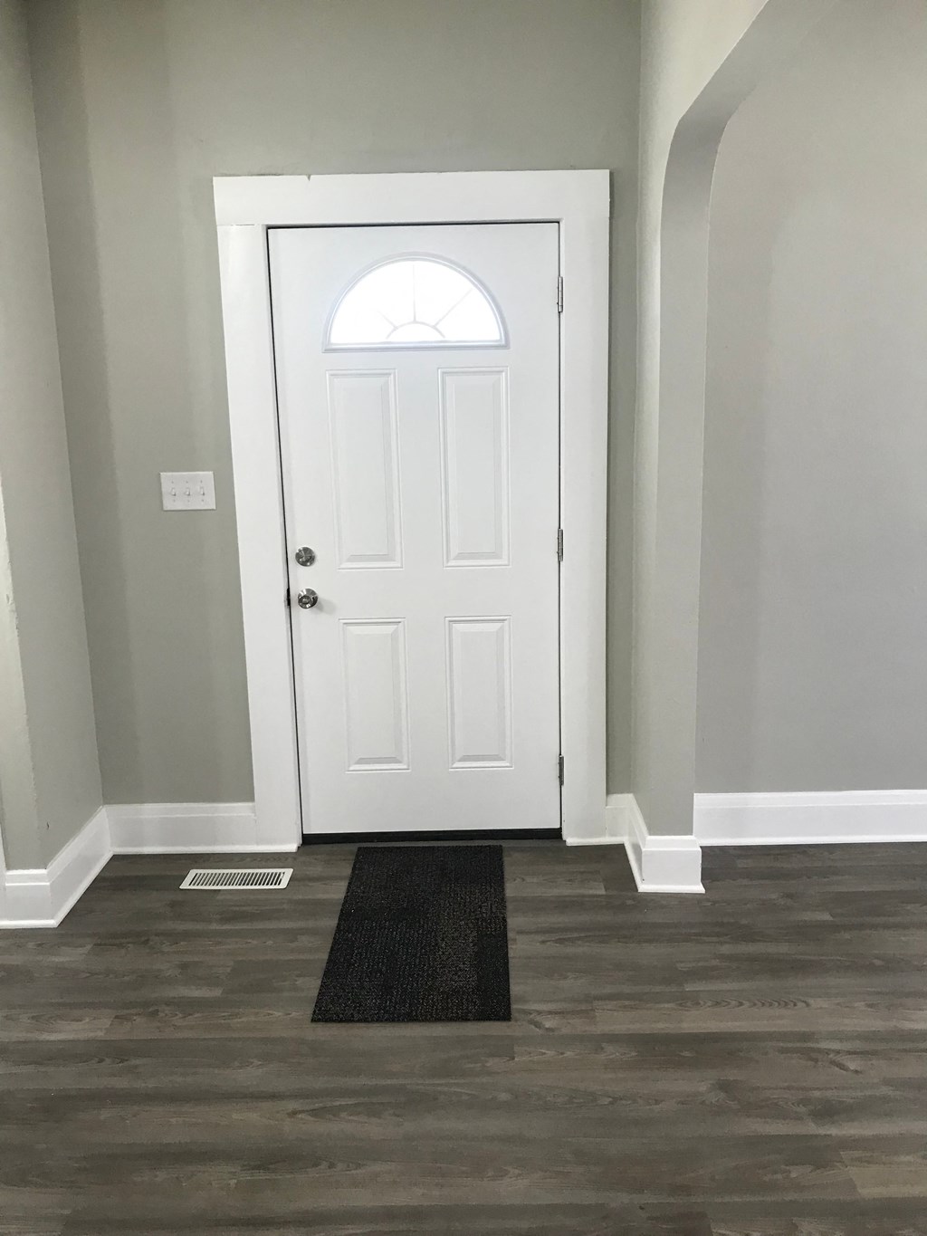 a white door with a window and a black rug in a room with grey walls