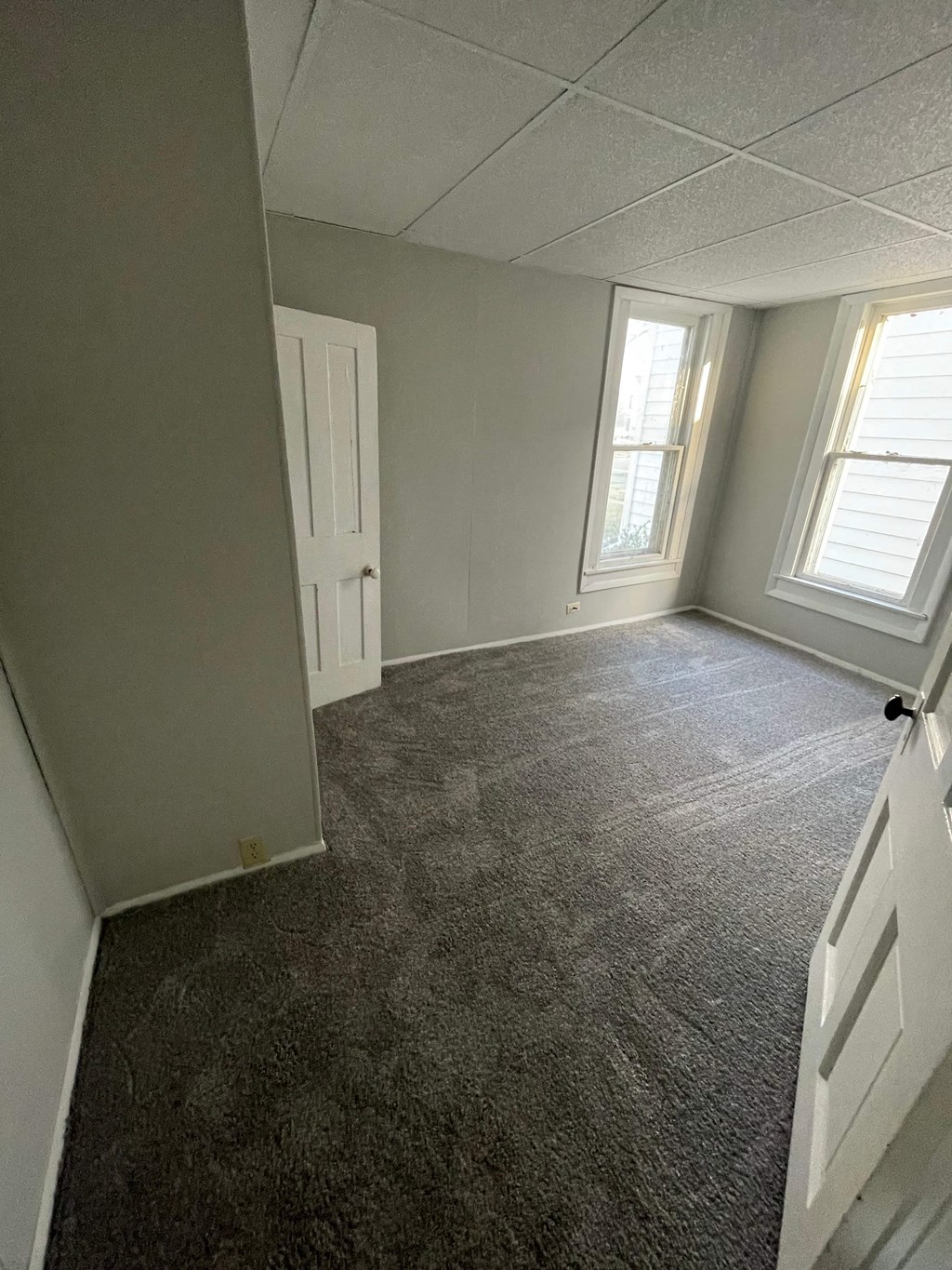 an empty bedroom with a carpeted floor and two windows