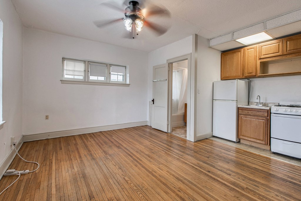 an empty living room with a kitchen and a ceiling fan