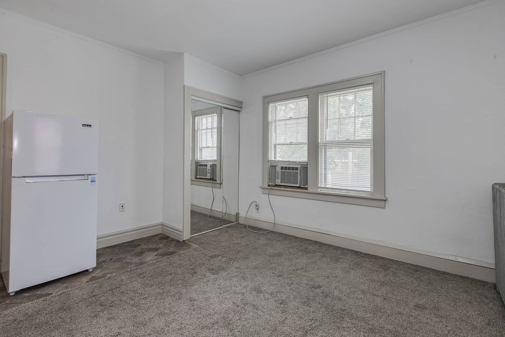 an empty room with a refrigerator and two windows