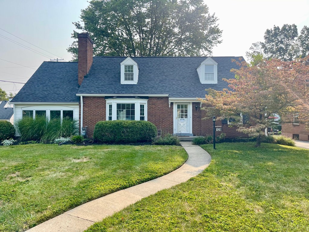A house with a brick facade and a white door is surrounded by a well-kept lawn.