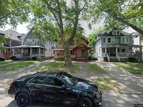 A black car is parked on a street in front of a house.